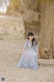 A woman in a blue dress sitting next to a tree.