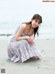 A woman in a long dress sitting on the beach.