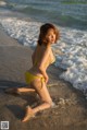 A woman in a yellow bikini sitting on the beach.