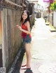 A young woman standing on a sidewalk next to a wall.