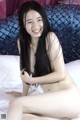 A naked asian woman sitting on a bed smiling.