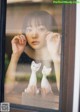 A woman looking out of a window at two white cats.