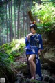 A woman in a blue kimono standing on a rock in the woods.