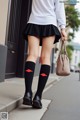 A woman in a white shirt and black skirt is walking down the street.