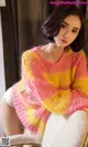 A woman sitting on a chair wearing a pink and yellow sweater.